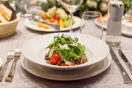 Fresh salad with tomatoes, beef, lettuce and arugula on plates in restaurant.