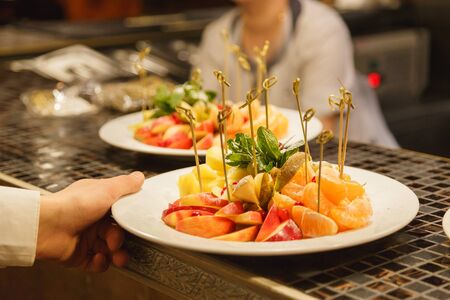 Fruit slicing on a white plate in the hands of a waiterの写真素材