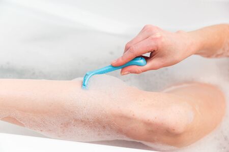 A woman in the bathroom shaves her legs with a razor. Close-up of a hand with a razorの写真素材