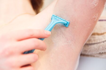 Woman in the bathroom shaves her armpits with a razor. Close-up hand with a shaver.の写真素材