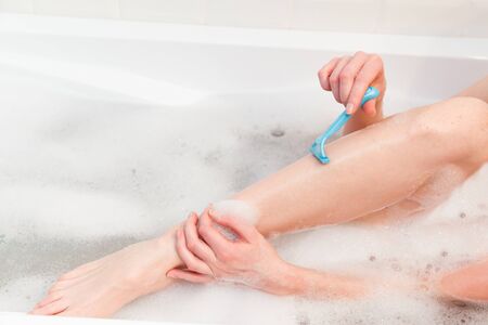 A woman in the bathroom shaves her legs with a razor. Close-up of a hand with a razorの写真素材