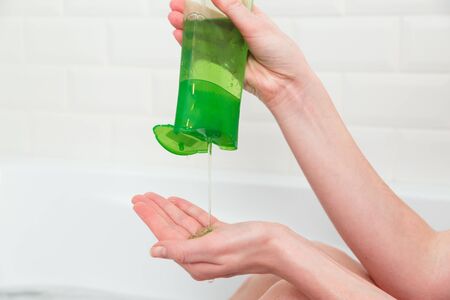 Woman pours green shampoo from a bottle into her palm. Bathroom, hair and body care. Eco-friendly cosmetics.の写真素材