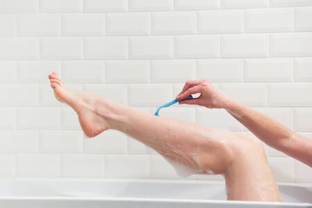 A woman in the bathroom shaves her legs with a razor. Close-up of a hand with a razorの写真素材