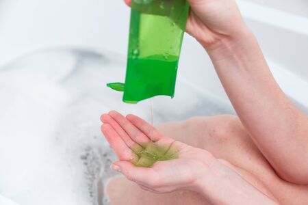 Woman pours green shampoo from a bottle into her palm. Bathroom, hair and body care. Eco-friendly cosmetics.の写真素材