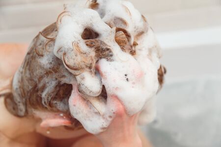 Redhead young woman washing her hair with shampoo sitting in bath.の写真素材