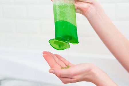 Woman pours green shampoo from a bottle into her palm. Bathroom, hair and body care. Eco-friendly cosmeticsの写真素材