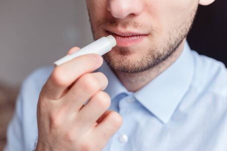 Man applying hygienic lipstick on lips to revive chapped lips and avoid dry, closeup. Man use protective cosmetics for careの写真素材