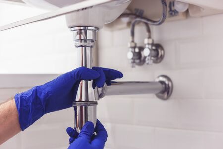 Plumber repairs and maintains chrome siphon under the washbasin. Plumber at work in bathroom, plumbing assemble and install concept.の写真素材