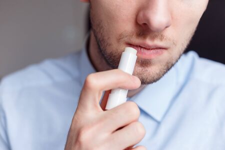 Man applying hygienic lipstick on lips to revive chapped lips and avoid dry, closeup. Man use protective cosmetics for careの写真素材
