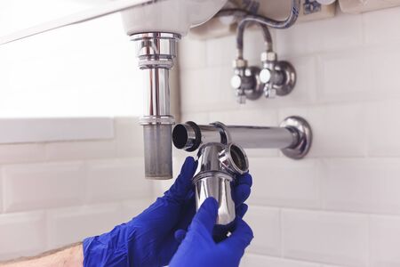 Plumber repairs and maintains chrome siphon under the washbasin. Plumber at work in bathroom, plumbing assemble and install concept.の写真素材