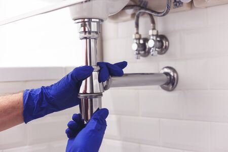 Plumber repairs and maintains chrome siphon under the washbasin. Plumber at work in bathroom, plumbing assemble and install concept.の写真素材