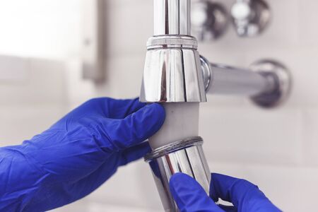 Plumber repairs and maintains chrome siphon under the washbasin. Plumber at work in bathroom, plumbing assemble and install concept.の写真素材
