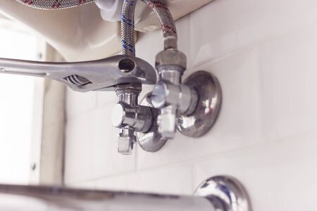 Plumber turns nut on angle valve under wash basin using spreading wrenchの写真素材