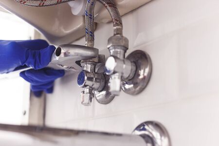 Plumber turns nut on angle valve under wash basin using spreading wrenchの写真素材