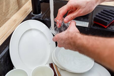 Washing dishes - man hands in gloves rinsing glass under running water in the sinkの写真素材