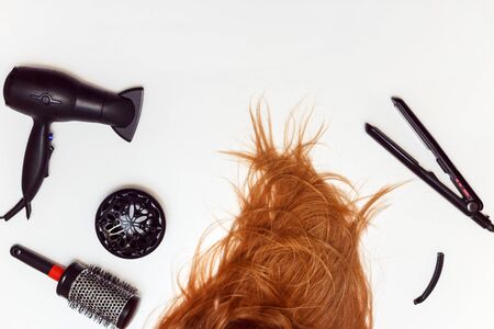 Disheveled red hair and hairdressing styling tools. Hair dryer, iron, comb and red hair on a white backgroundの写真素材