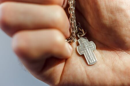 Silver cross in the hand with focus on the cross, shallow DOFの写真素材