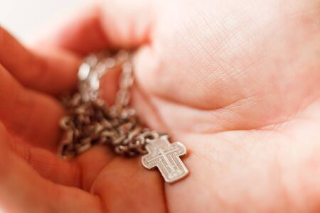 Silver cross in the hand with focus on the cross, shallow DOFの写真素材