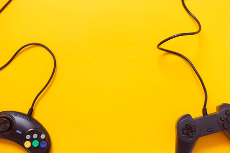 Two wired gamepads or video game controllers on yellow background. Top view, flat lay. Gaming,...
