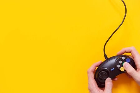 Man holding wired gamepad or video game controller on yellow background. Top view, flat lay.の写真素材