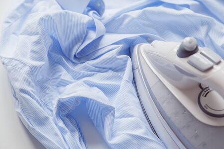 Blue cotton wrinkled and rumpled shirt ironing with iron. Tumble dryer after washing machineの写真素材