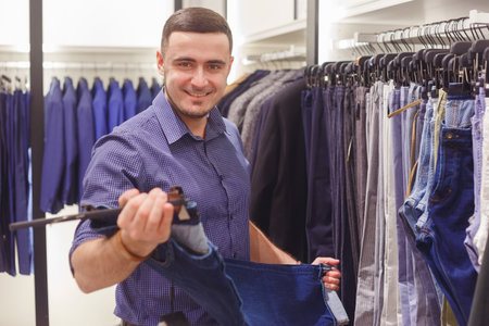 Man choosing classical trousers in fashion clothes shop.