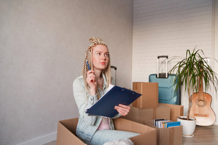 Beautiful woman sitting in box in casual clothes is packing her stuff into the boxes, making notes