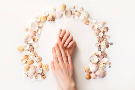 Womans hands with perfect manicure and seashells around. Top view photo isolated on white, flat layの写真素材