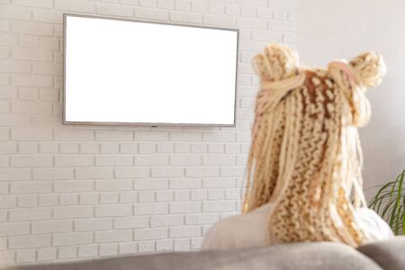 woman watching tv in living room on wall at home, white blank screen empty copy space, back viewの写真素材