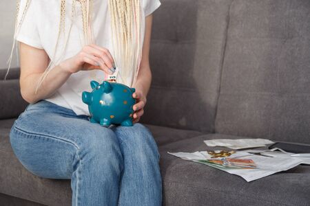 Young woman putting 10 euro into money box sitting on sofa at homeの写真素材