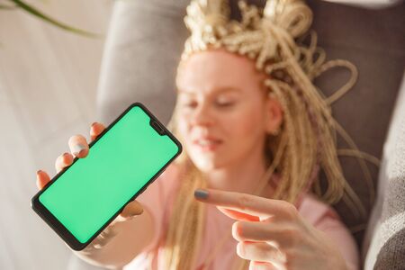 Young emotional blond woman shows smartphone with green copy space screen, focus on screenの写真素材