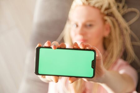 Young emotional blond woman shows smartphone with green copy space screen, focus on screenの写真素材