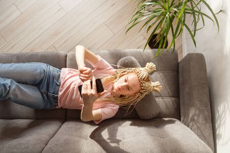 Woman use a smartphone while lying on a sofa. Top view.の写真素材