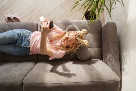 Woman use a smartphone while lying on a sofa. Top view.の写真素材