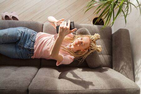 Woman use a smartphone while lying on a sofa. Top view.の写真素材