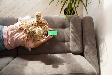 Woman with blond canecalons lying on a sofa uses smartphone with green screen for your image.の写真素材
