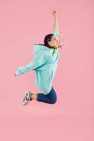 Happy girl with kanekalons weared in sports casual style jumping on pink isolated backgroundの写真素材