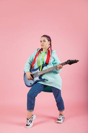 young and beautiful woman with electric guitar on pinkの写真素材