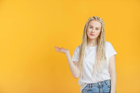 Beautiful 30 year old woman with braids kanekalon hairstyle point to copy space on yellow backgroundの写真素材