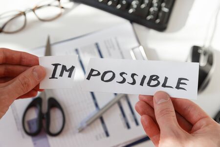 Businessman hands cutting the word impossible, letters im so it become possible. Success and motivation concept. Photo at workplace.の写真素材