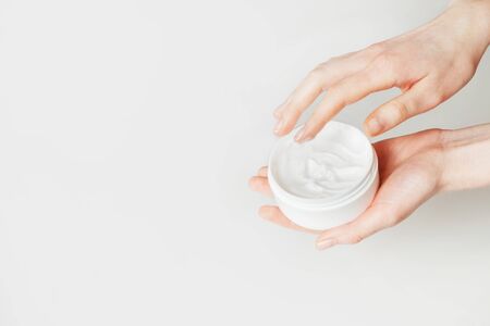Woman hand touch moisturizer white cream in jar. Isolated on white with copy space.の写真素材