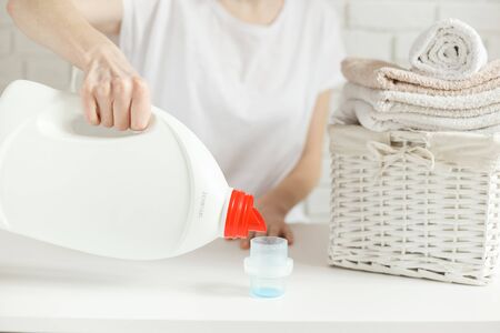Woman wants to pour detergent into cap on table, but bottle is empty, gel is over, close-up. Laundry conceptの写真素材