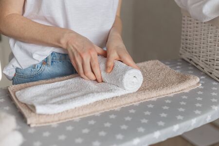 Woman rolling ironed clean towels standing at ironing board. Laundry service or cleaning housework conceptの写真素材