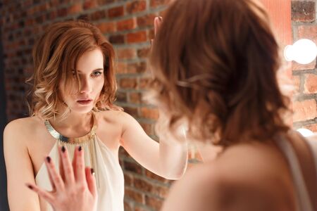 Beautiful red-haired woman intently desperate looks in the mirror.の写真素材