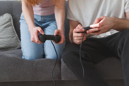 A young couple a girl and a guy with joysticks in their hands play on the console while sitting on the couchの写真素材