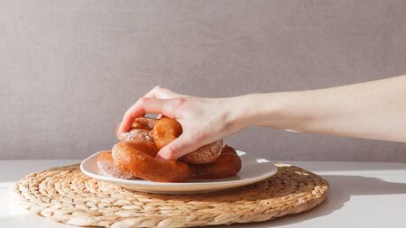 Glutton girl grabs donuts from a plate. Girls hand and plate with donuts.の写真素材