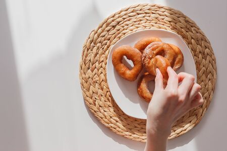 Glutton girl grabs donuts from a plate. Girls hand and plate with donuts. Natural lightの写真素材