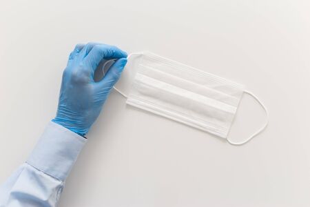 Doctor's hand in a protective glove and face mask on a white background. Epidemic concept.の写真素材