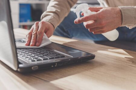Man disinfects his laptop, cleaning keyboard . Wipe with rubbing alcohol spray and disinfectant.の写真素材