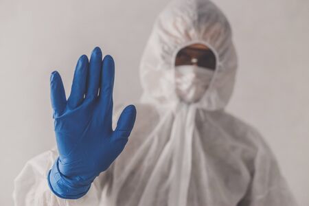 Epidemic. Man in protective suit, mask gestures stop by hand in gloveの写真素材